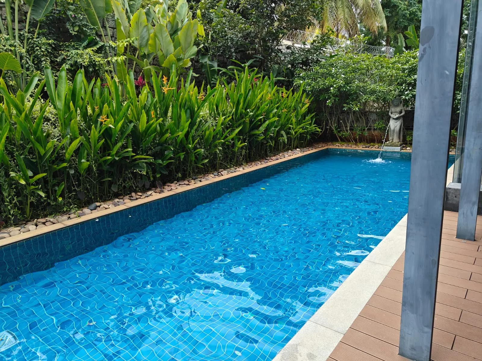 A tiled swimming pool framed by tropical greenery beside a contemporary Yelahanka villa